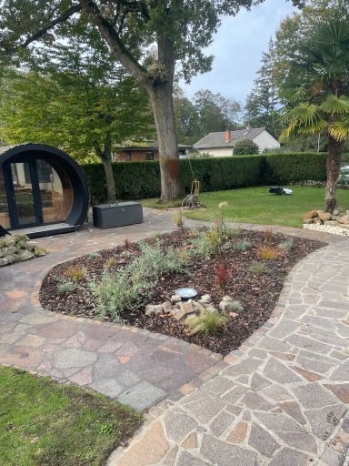 Garten mit bunten Pflanzen, einem runden Pavillon und einem gepflasterten Weg.