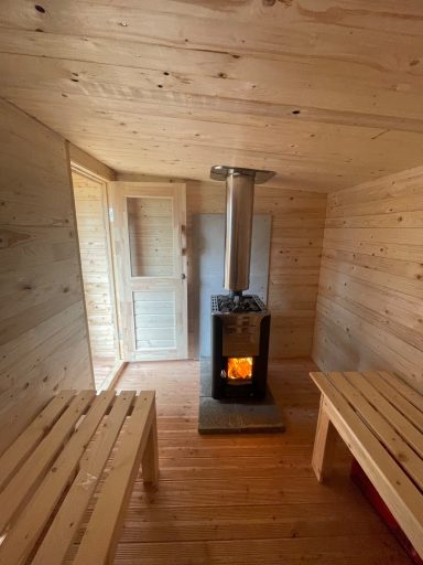 Gemütlicher Innenraum mit Holzofen und zwei Holzbankbänken.