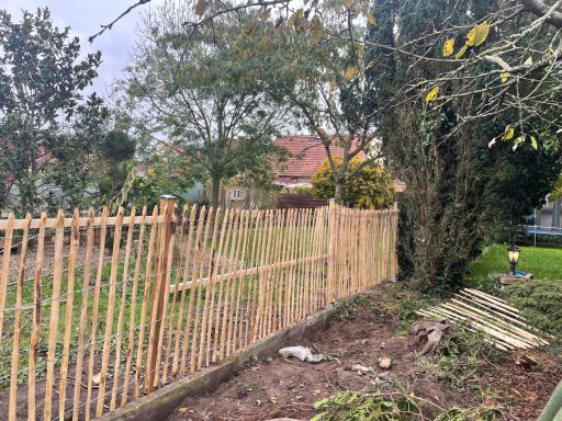 Holzlattenzaun an einem Garten mit Bäumen im Hintergrund.